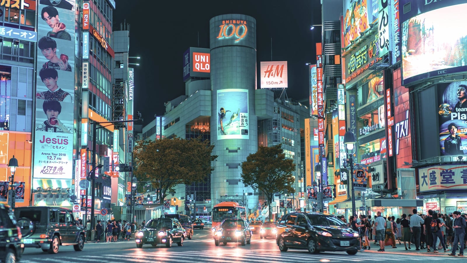 A neon-lit Tokyo street with large screens and traffic