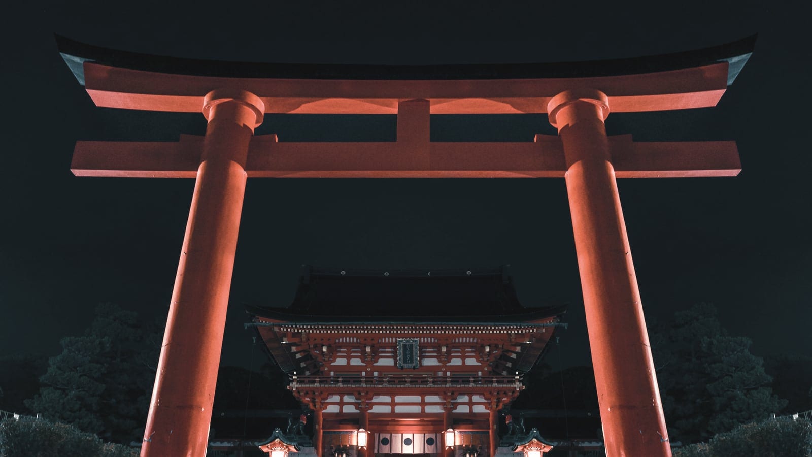A red torii gate glowing against a dark shrine approach