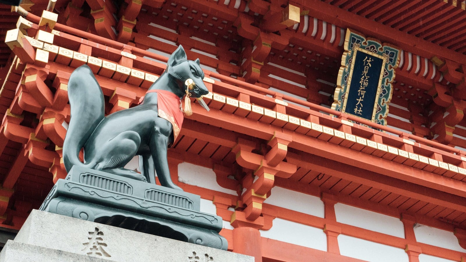 Fox statues in front of a vivid red Inari shrine building